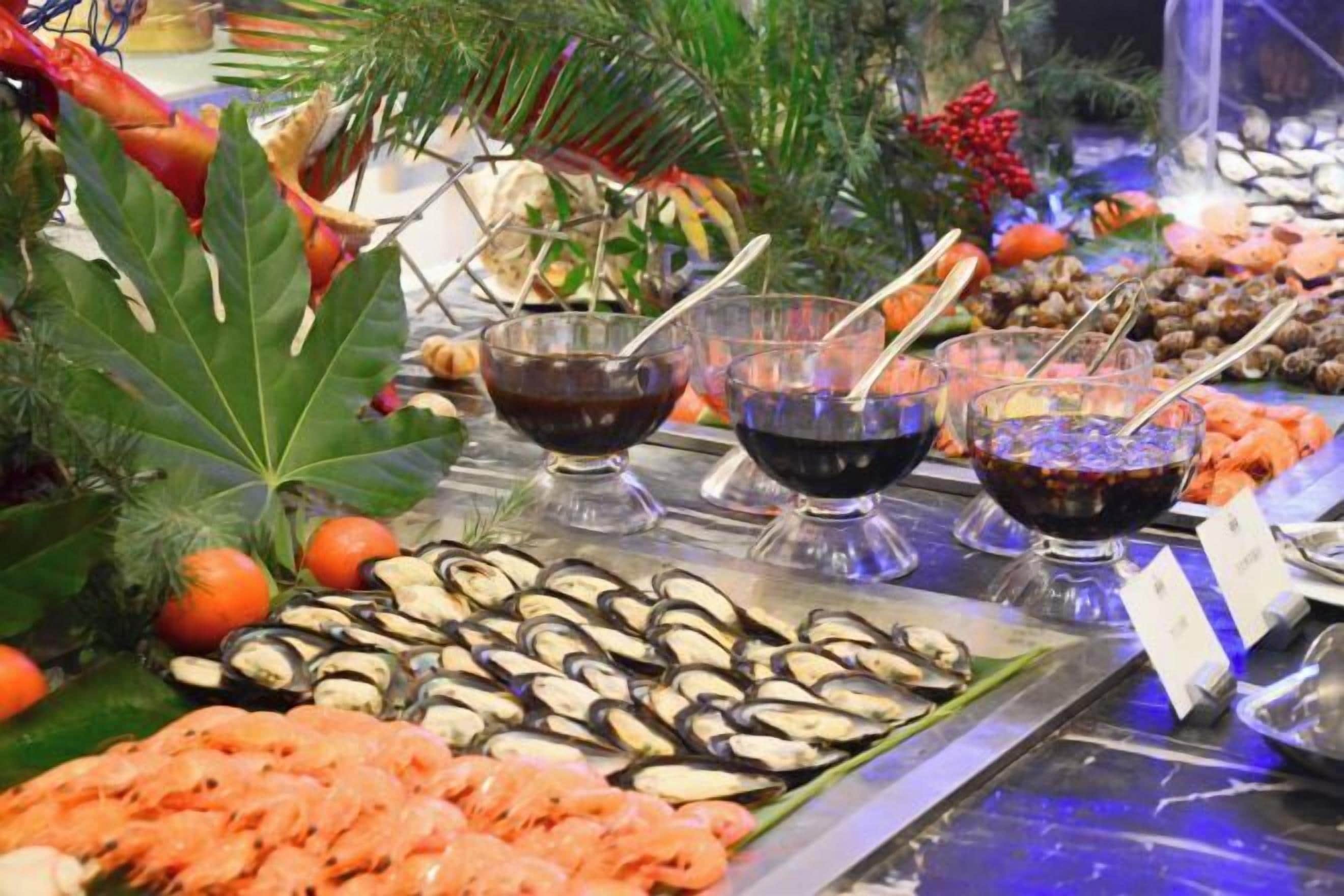 A buffet with seafood, including shrimp and mussels, and three bowls of sauce.
