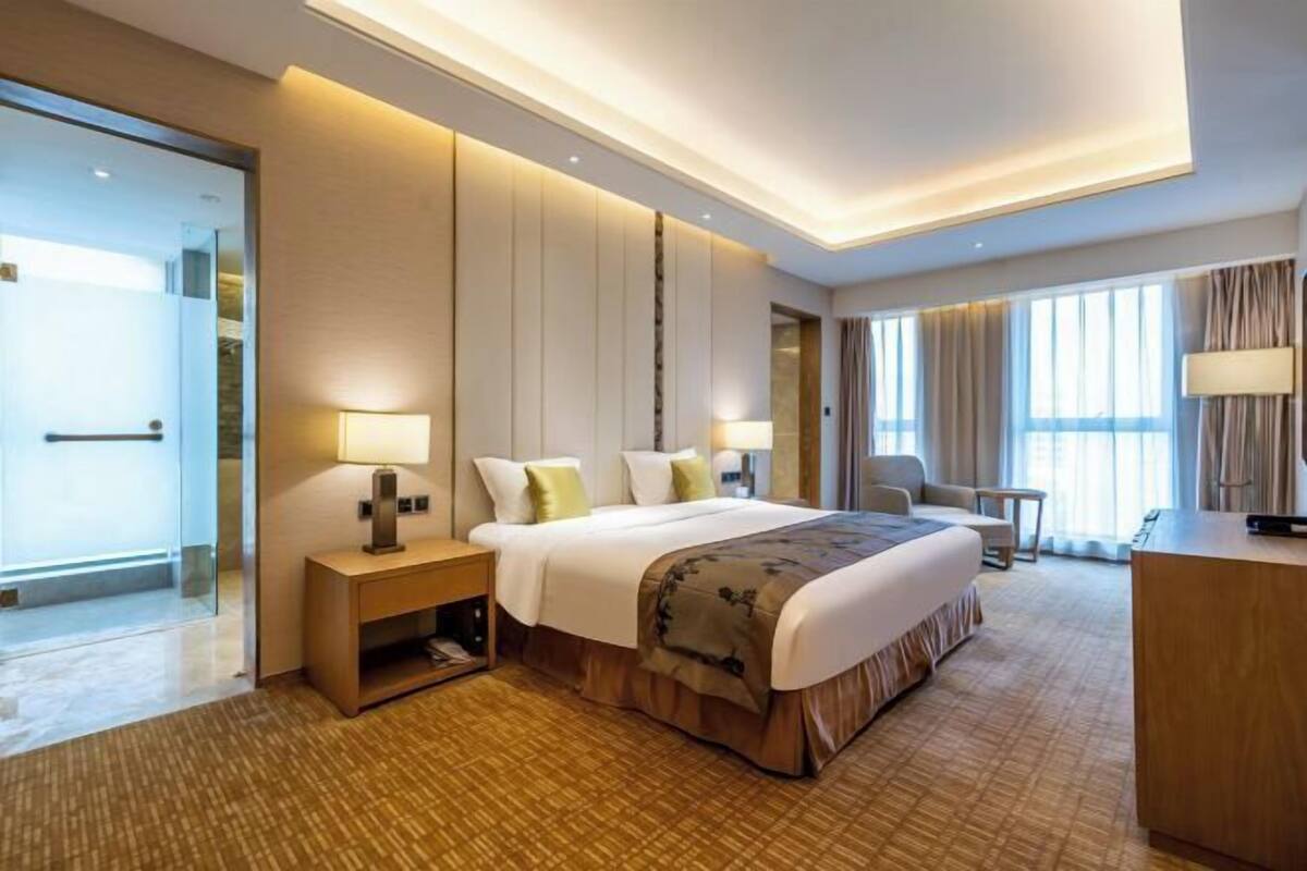 Un hotel moderno con una cama grande, mesitas de noche, un escritorio y vistas a la ciudad a través de amplios ventanales.