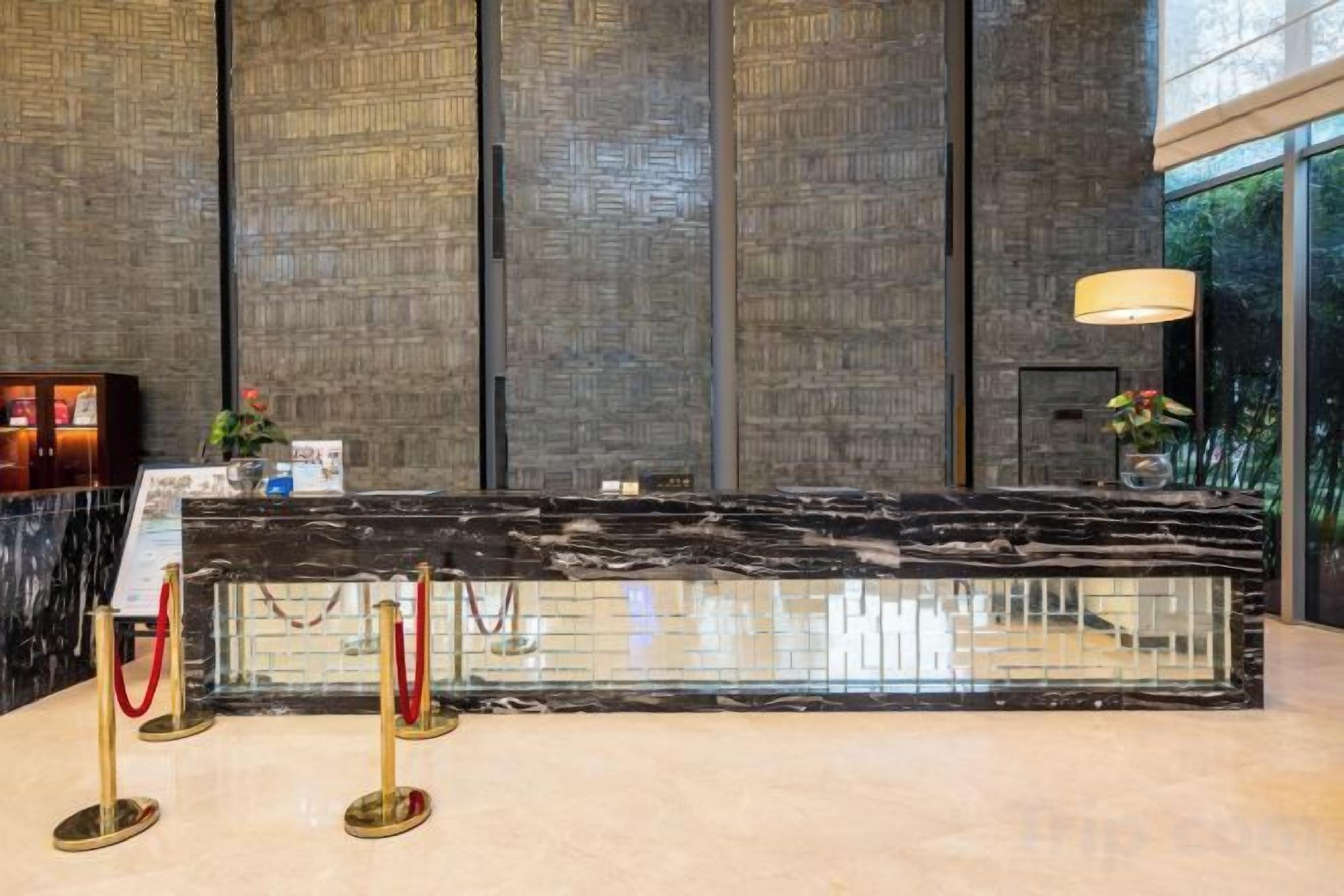 A reception desk with a marble top, a red rope barrier, and a wall with vertical panels.
