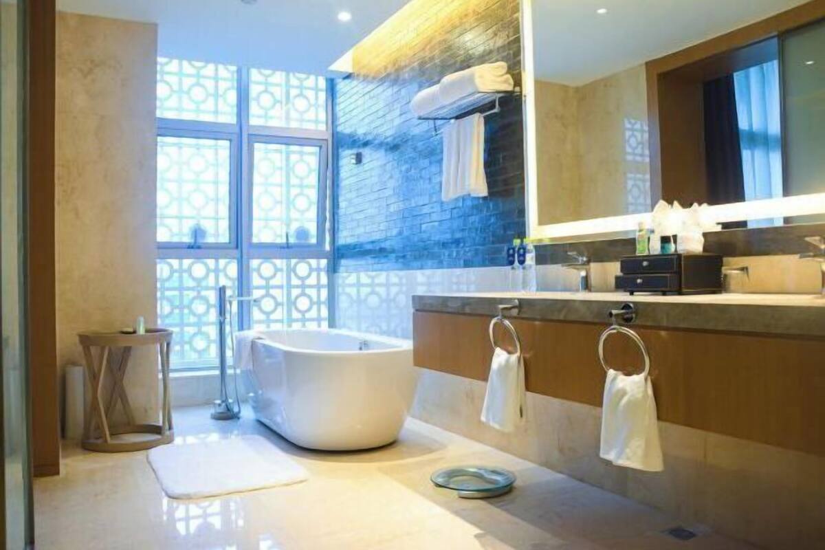 Un baño moderno con una bañera independiente, un espejo grande y un ventanal con celosía decorativa.