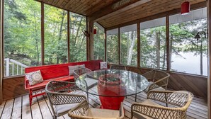 Una terraza de madera con una mesa de vidrio rodeada de sillas de mimbre y un banco rojo.