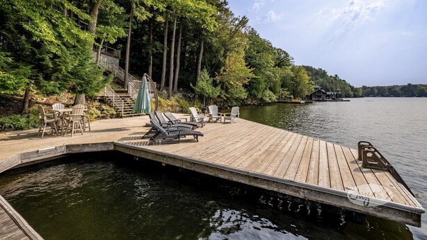 Un muelle de madera se adentra en un lago, rodeado de árboles densos y un pequeño edificio con una escalera.