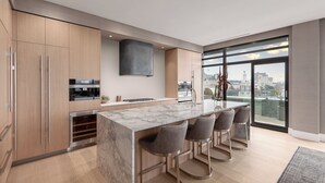 Une cuisine moderne dotée d’un îlot en marbre, de tabourets de bar et offrant une vue sur la ville grâce à de grandes fenêtres.