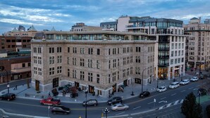 Un bâtiment historique avec une entrée d’angle, un café Starbucks et une rue animée où circulent des voitures et des piétons.