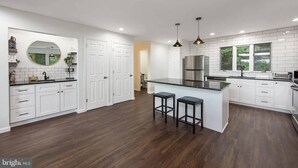 A modern kitchen with white cabinetry, a central island with stools, a large window, and a stainless steel refrigerator. - Pocono Mountains Camelback Retreat Ski-in Ski-out (Tannersville)