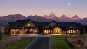 A large, modern house with a driveway and a well-maintained lawn, set against a mountainous backdrop. - Basecamp Stays: Lux Retreat, Teton Views, 3 Acres! (Tetonia)