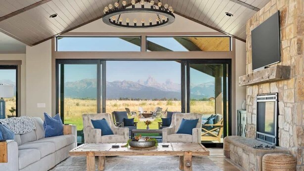 A spacious living room with a large window offering a mountain view, a fireplace, and a cozy seating area. - Basecamp Stays: Lux Retreat, Teton Views, 3 Acres! (Tetonia)