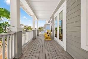 A covered wooden deck with a railing, two rocking chairs, and a view of neighboring houses.