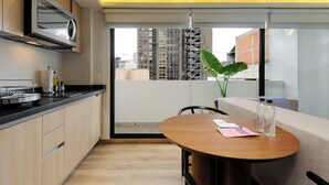 Una cuina moderna amb microones integrat, zona de menjador amb taula rodona i vista a la ciutat a través d'una finestra gran.