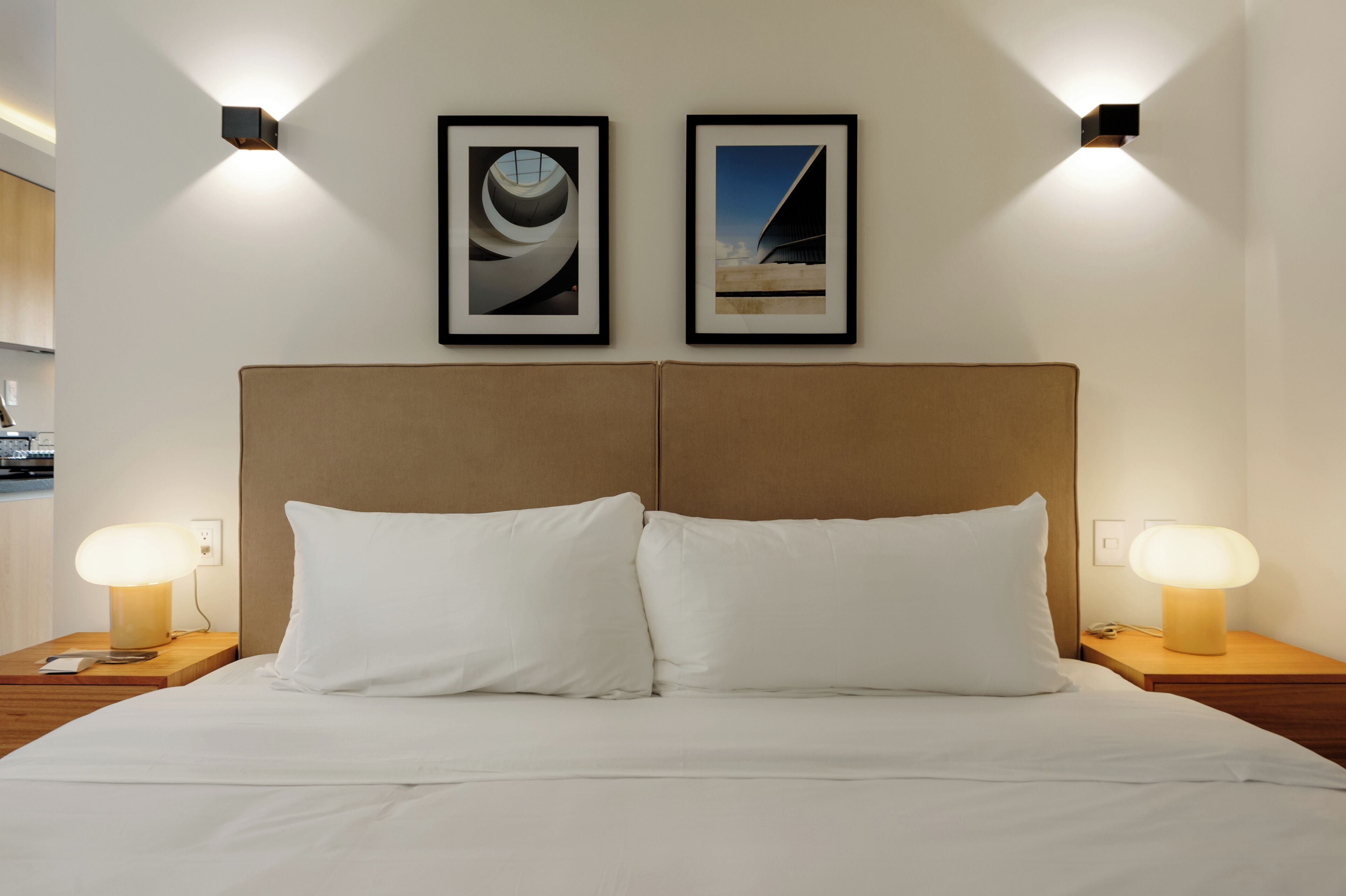 A hotel room with a large bed, two bedside lamps, and two framed pictures on the wall.