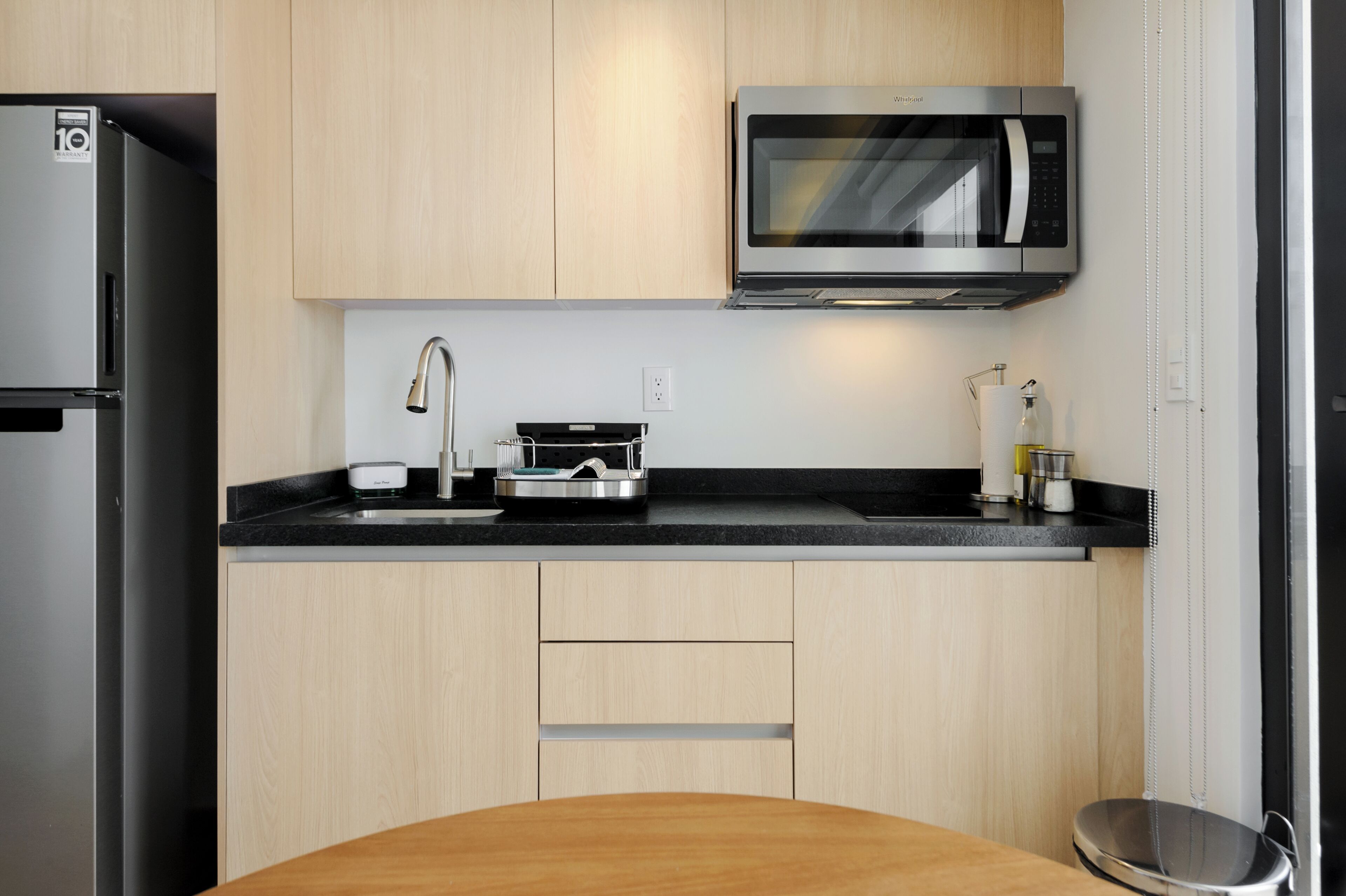 Una cocina moderna con un refrigerador de acero inoxidable, un microondas, un lavamanos y armarios de madera.