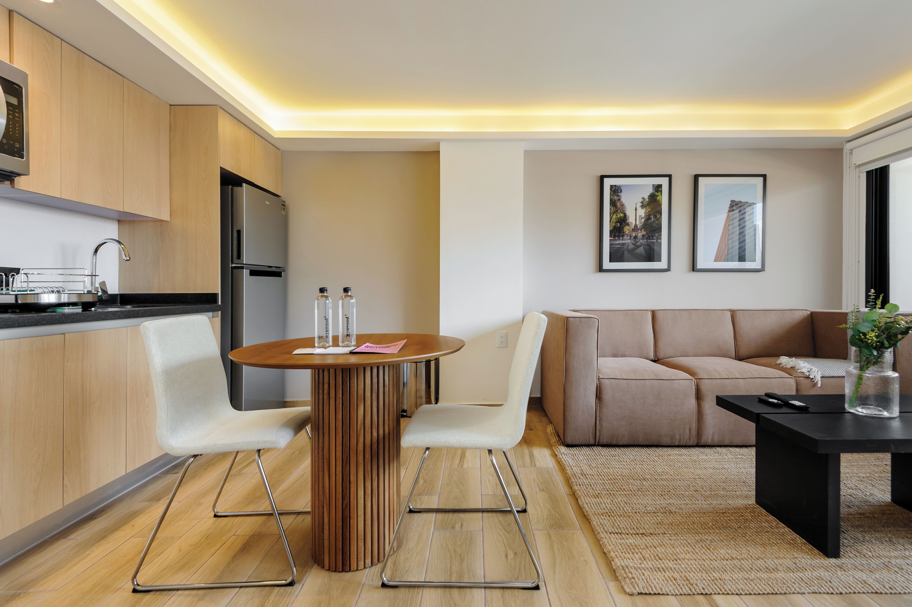 A modern kitchen with wooden cabinets, a stainless steel refrigerator, and a dining area with a round wooden table and white chairs.
