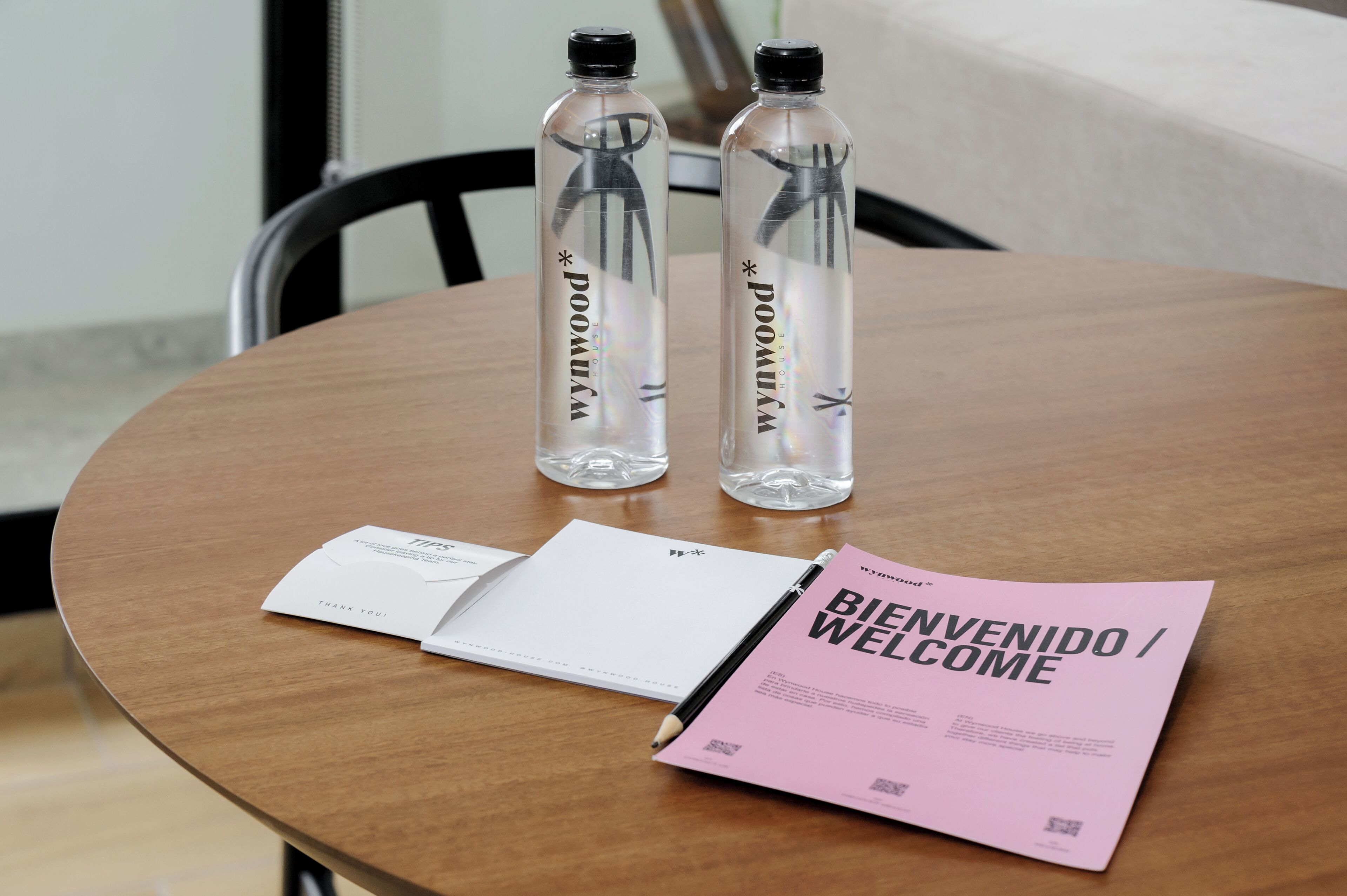 A wooden table with two clear water bottles, a white notepad, and a pink welcome card.
