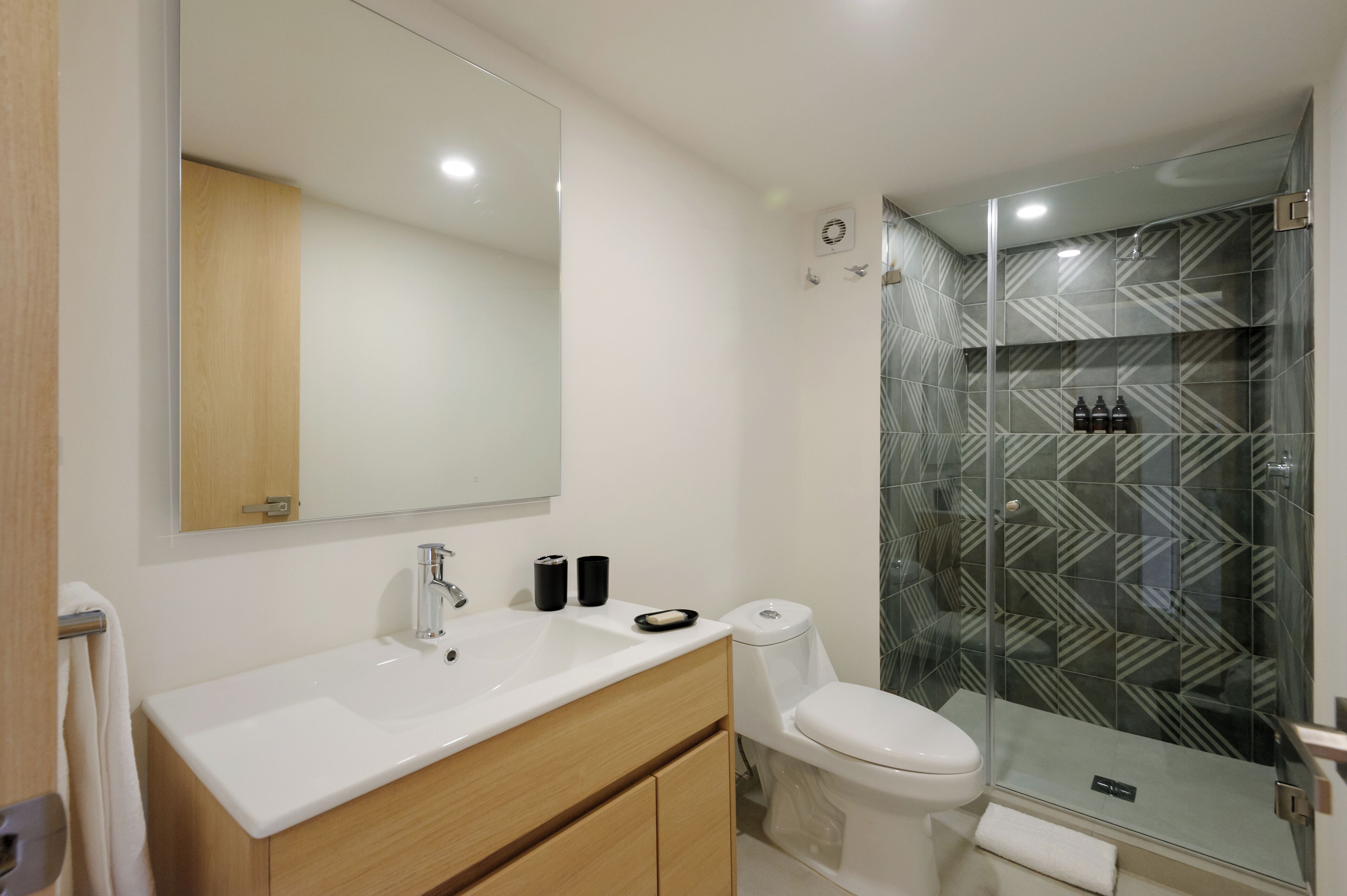 A modern bathroom with a white sink, wooden vanity, and a glass shower enclosure with patterned tiles.
