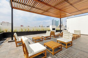 A rooftop terrace with wooden furniture and a view of the city skyline.