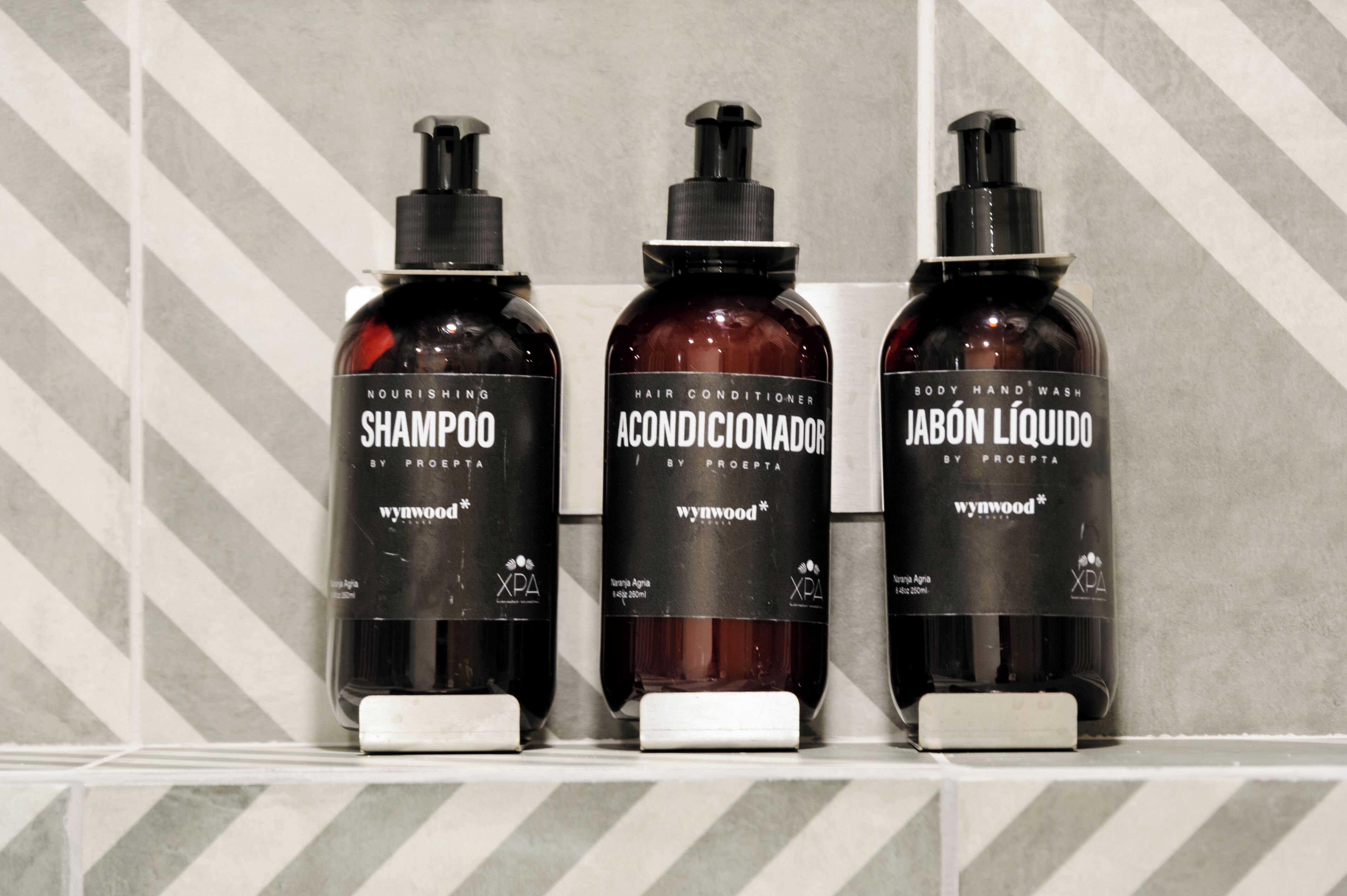Trois bouteilles de produits de soins capillaires de la marque Wynwood, posées sur une étagère carrelée.