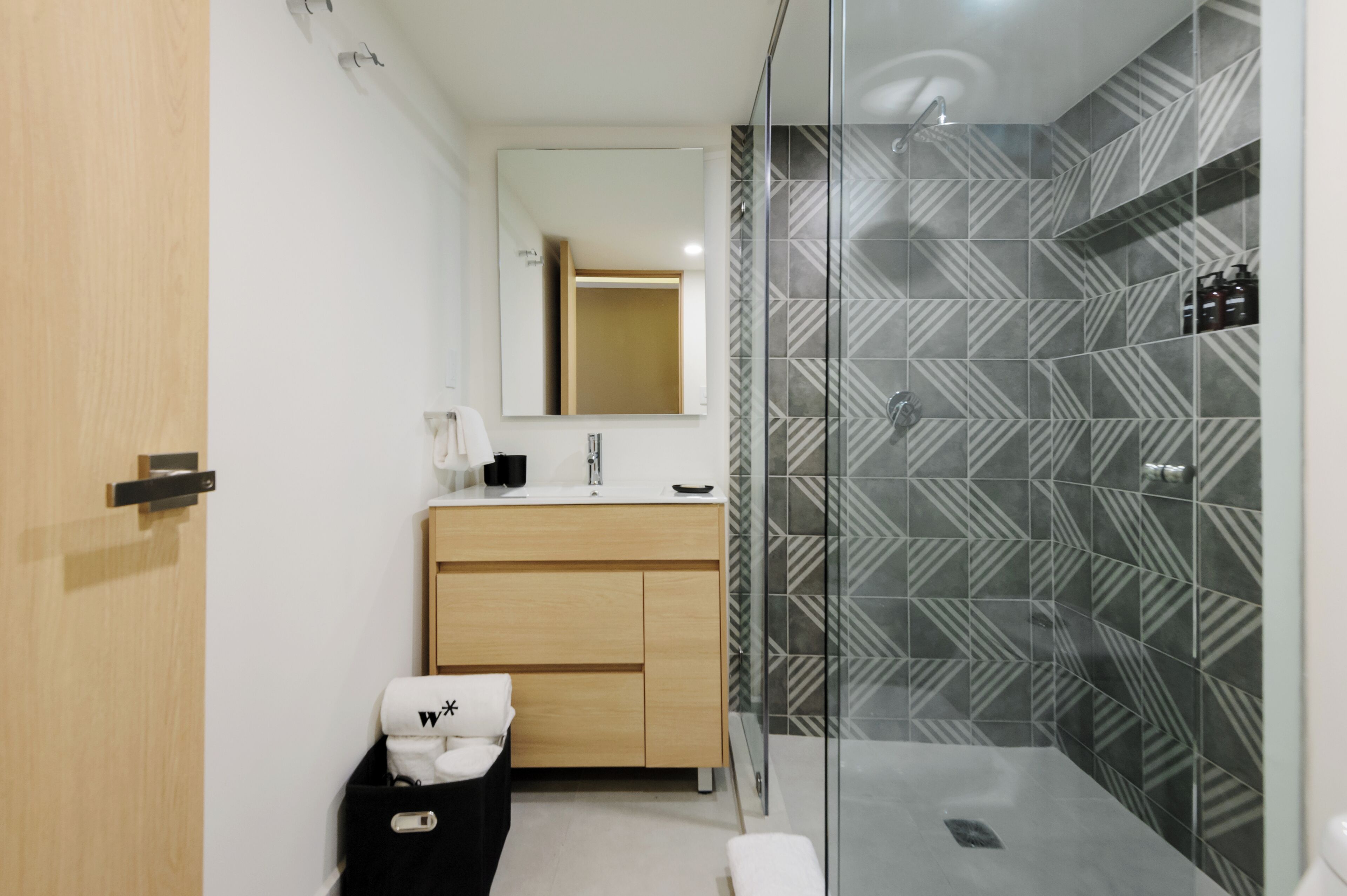 Une salle de bain moderne avec un meuble-lavabo en bois, un grand miroir et une douche aux carreaux décorés.