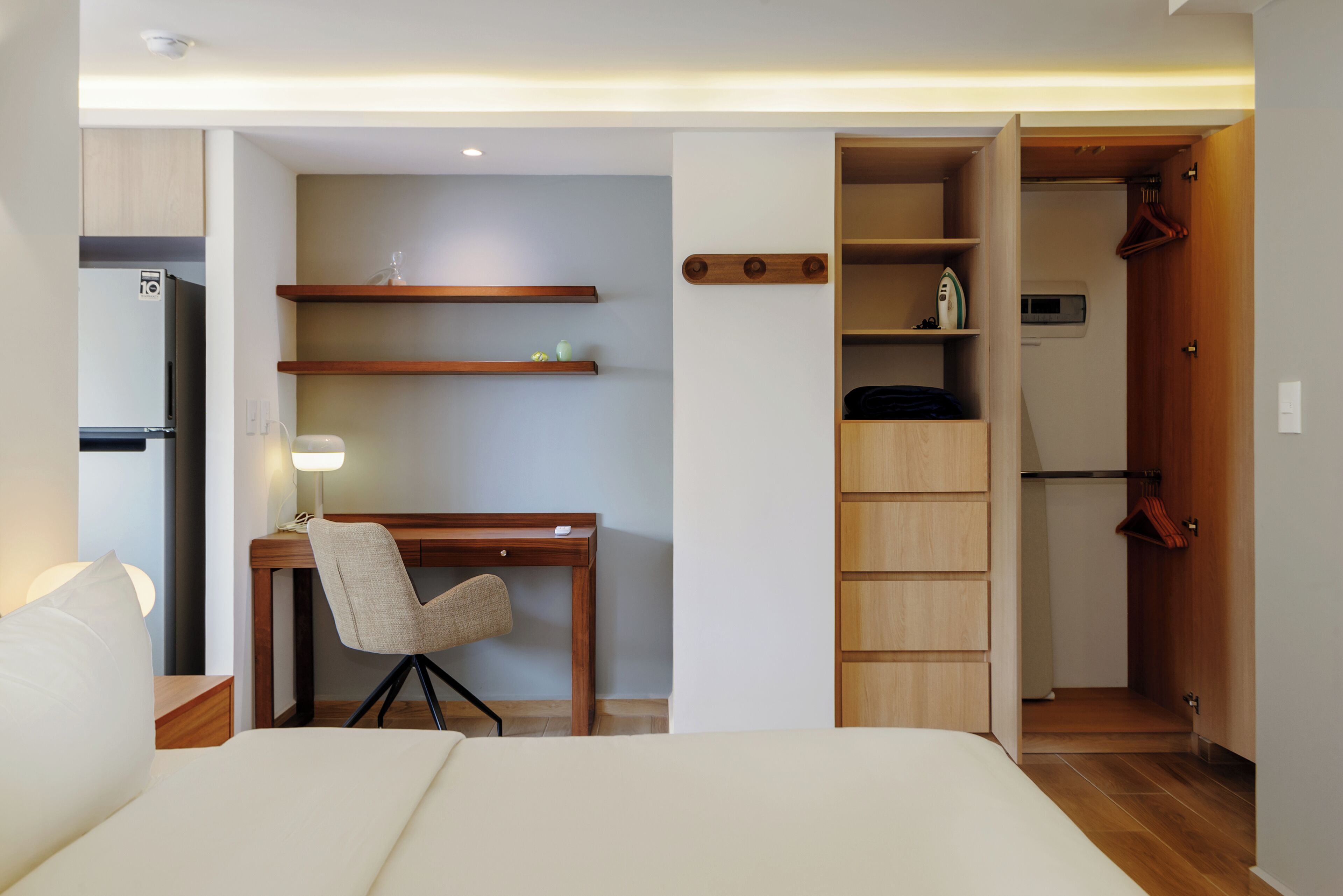 Una camera d'albergo compatta con un letto, una scrivania con sedia, un armadio e un angolo cottura.