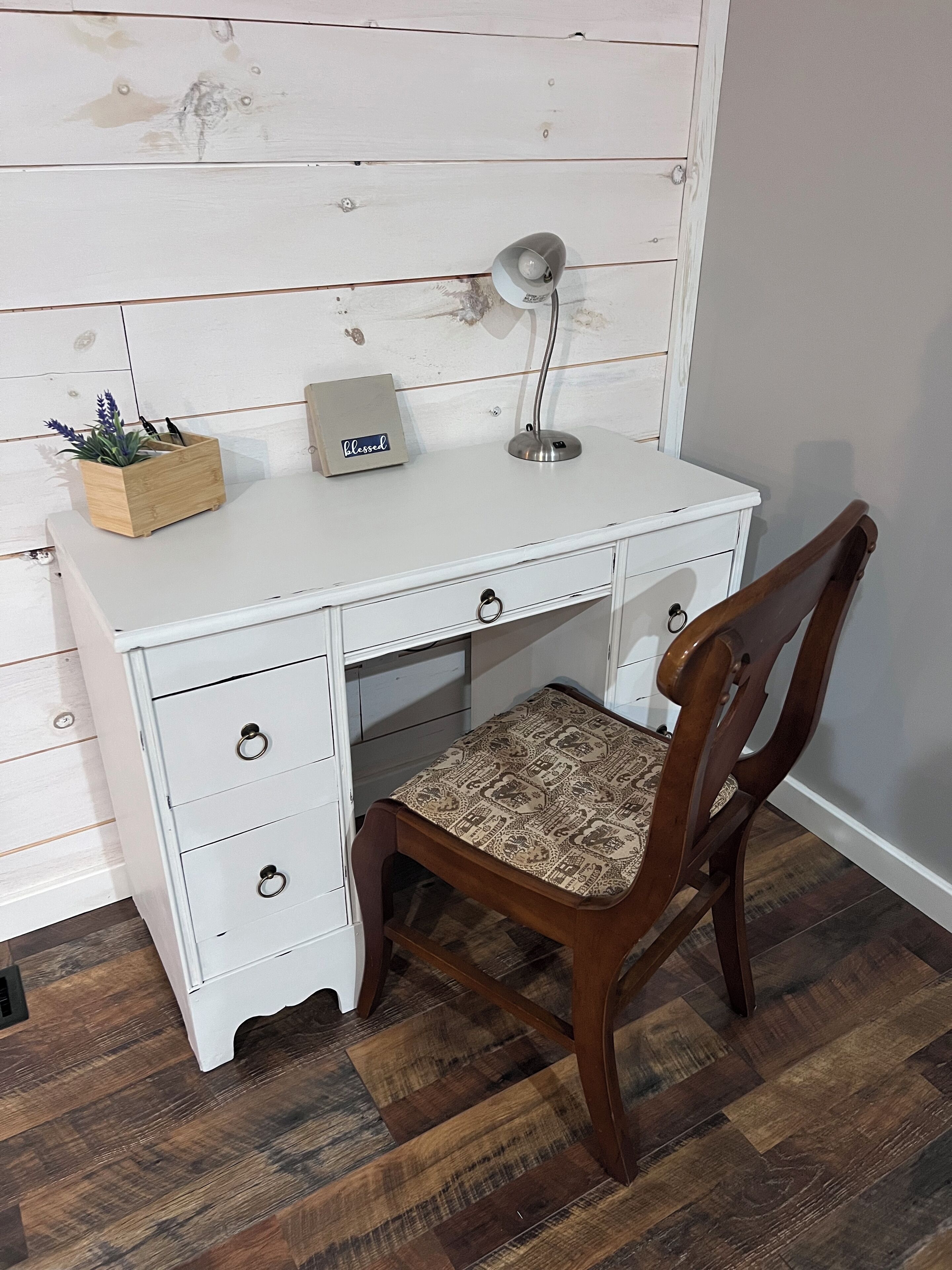 Un bureau blanc avec des tiroirs, une lampe et un support pour plante.