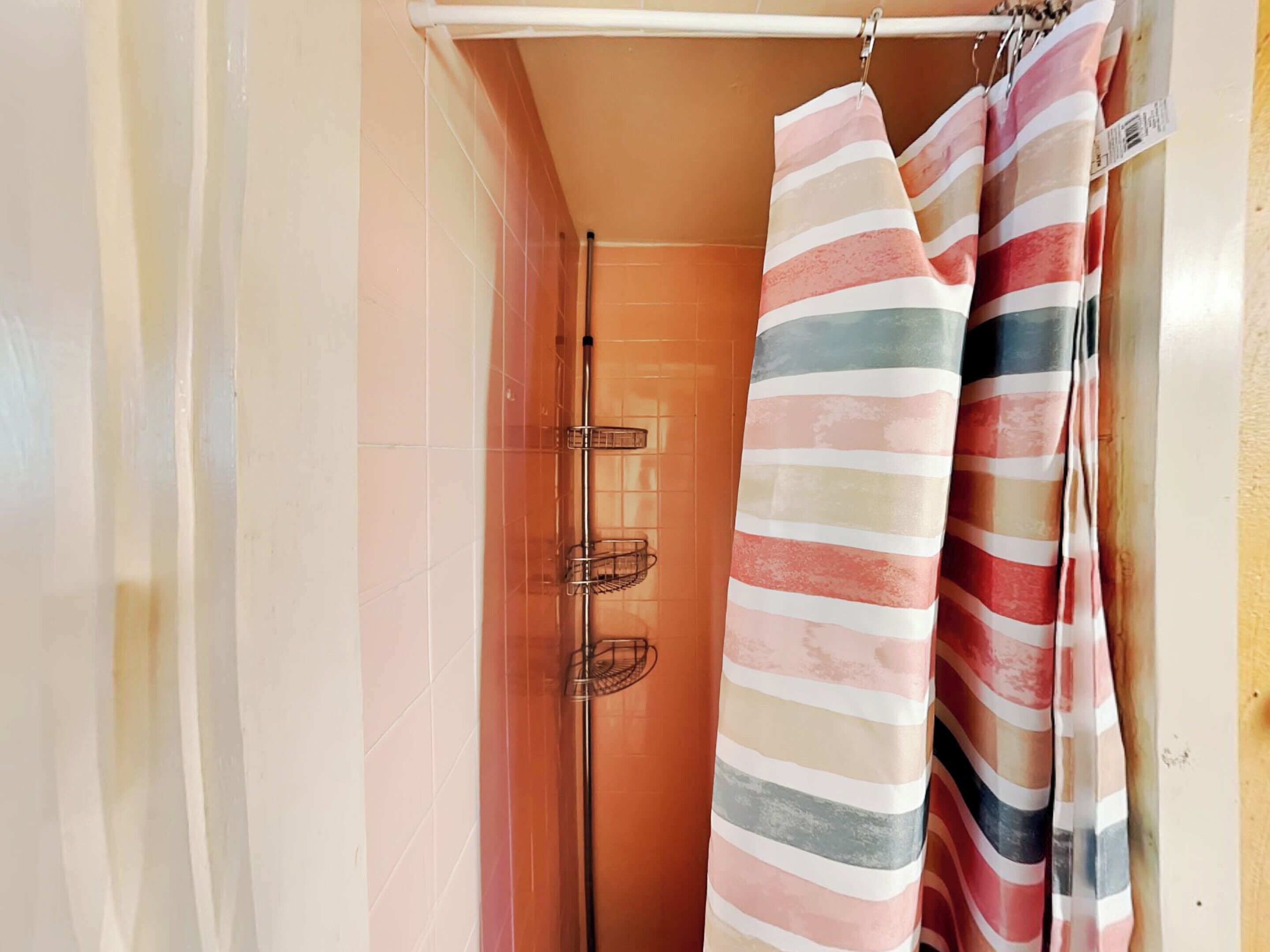 Un baño con zona de ducha, un perchero con toallas a rayas y pared de azulejos.