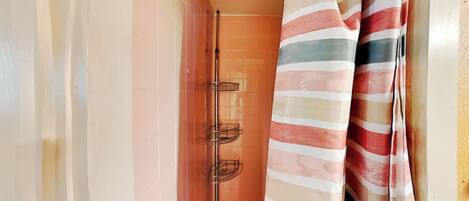Un baño con zona de ducha, un perchero con toallas a rayas y pared de azulejos.