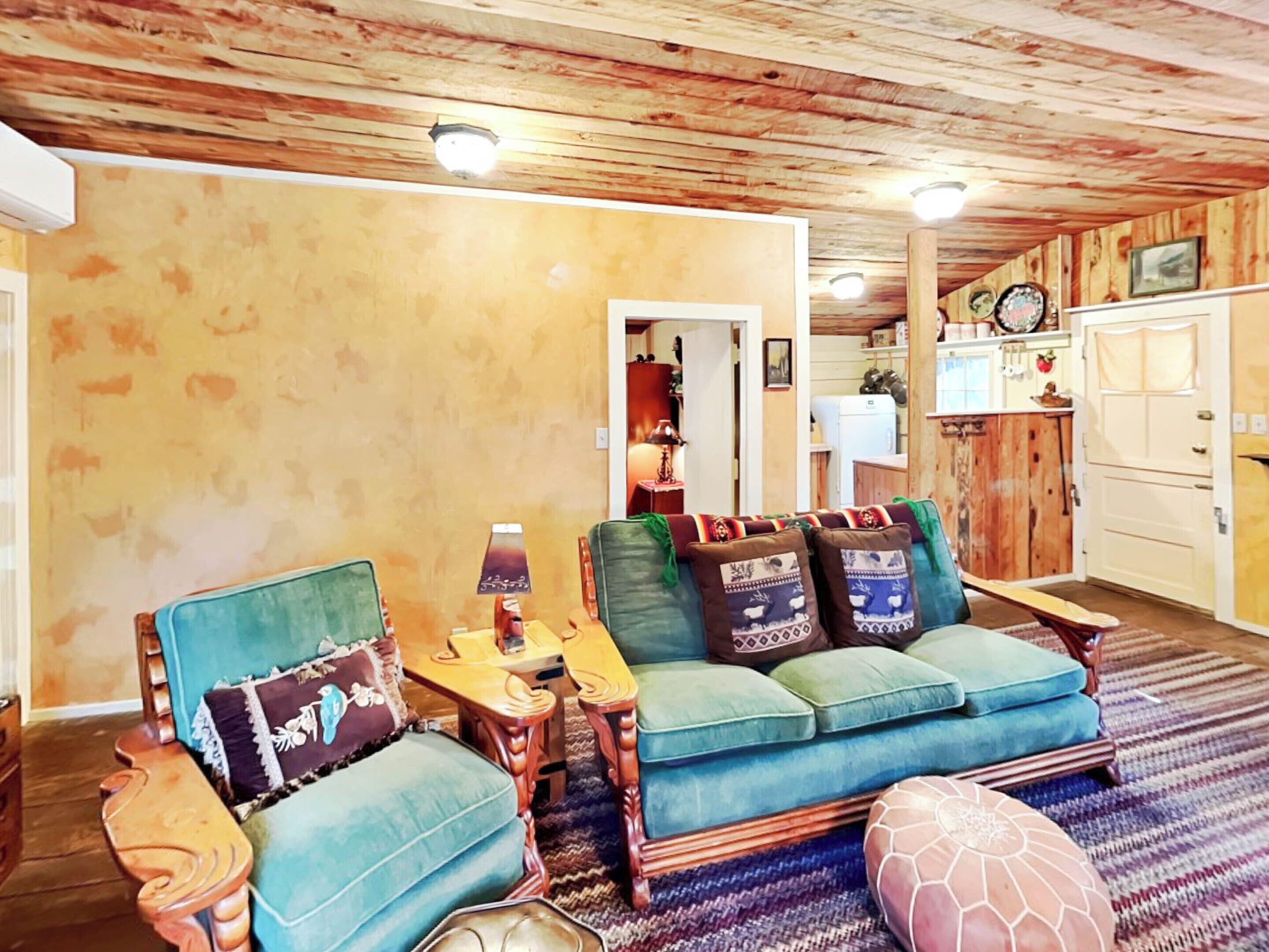 A cozy living room with a wooden ceiling, a blue sofa set, and a small wooden table with a lamp.