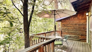 Une terrasse en bois avec une table et des chaises, entourée d’arbres.