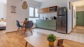 Een moderne keuken met een ingebouwde magnetron, een koelkast van roestvrij staal en een eethoek met een houten tafel en stoelen.