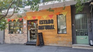 Una fachada de madera, un letrero que dice "ESTADO NATURAL" y una puerta verde con un portón metálico.