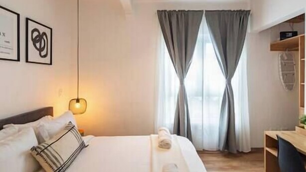 Una habitación de hotel moderna con una cama bien hecha, un escritorio y un amplio ventanal con cortinas.