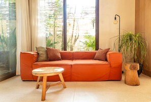 Une pièce avec une grande fenêtre, un canapé, une petite table en bois et une plante en pot.
