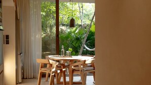 A room with a round wooden table and chairs, a hammock, and a view of greenery outside. - Apartment with Private Pool and Garden | •TEVA 1A (Tulum)