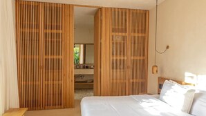 A bedroom with a bed, a wooden bench, and a sliding door leading to a bathroom. - Apartment with Private Pool and Garden | •TEVA 1A (Tulum)