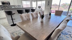 Un vaste espace dédié à la salle à manger, avec une grande table en bois, six chaises rembourrées et un tapis à motifs.
