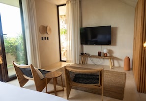 A room with two wicker chairs, a television, a small table, and a view through a glass door.