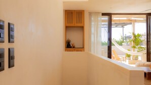 Un intérieur moderne avec une colonne centrale, une étagère en bois et une vue sur un espace extérieur agrémenté de plantes et d’un hamac.