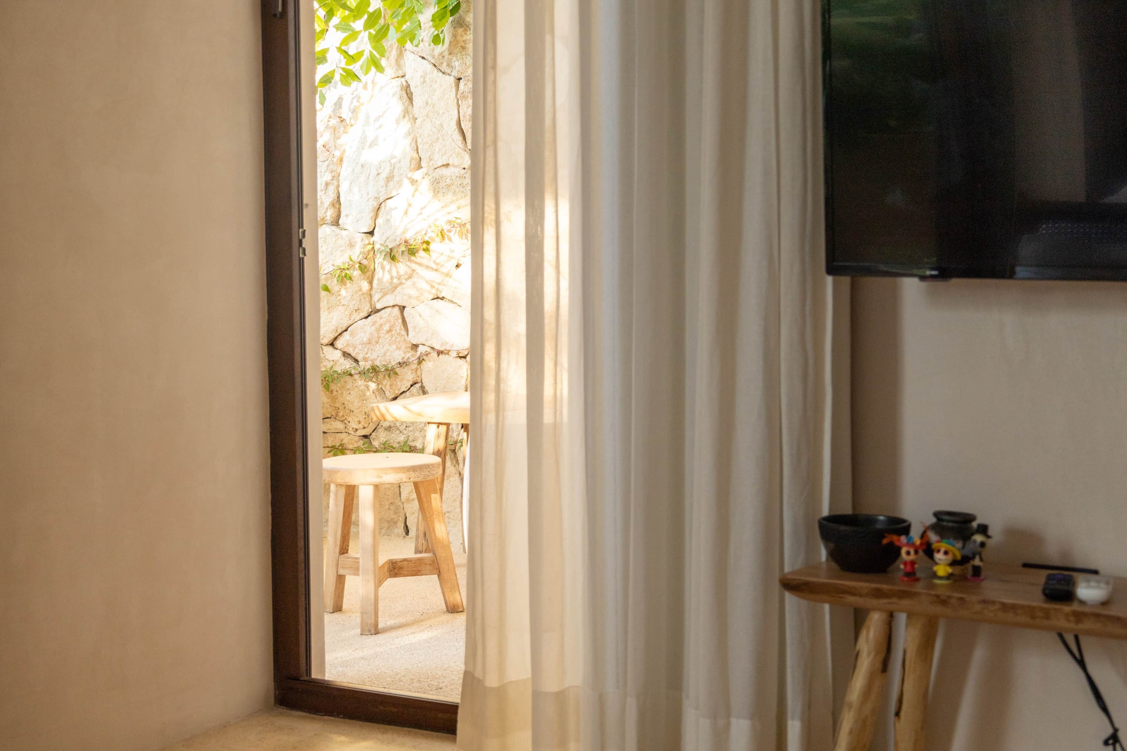A room with a stone wall, a wooden stool, a table with a bowl and figurines, and a TV mounted on the wall.