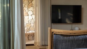 Une pièce avec un mur en pierre, un téléviseur fixé au mur et un lit avec une tête de lit.