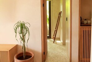 A hallway with a potted plant, a wooden ladder, and a tiled floor.