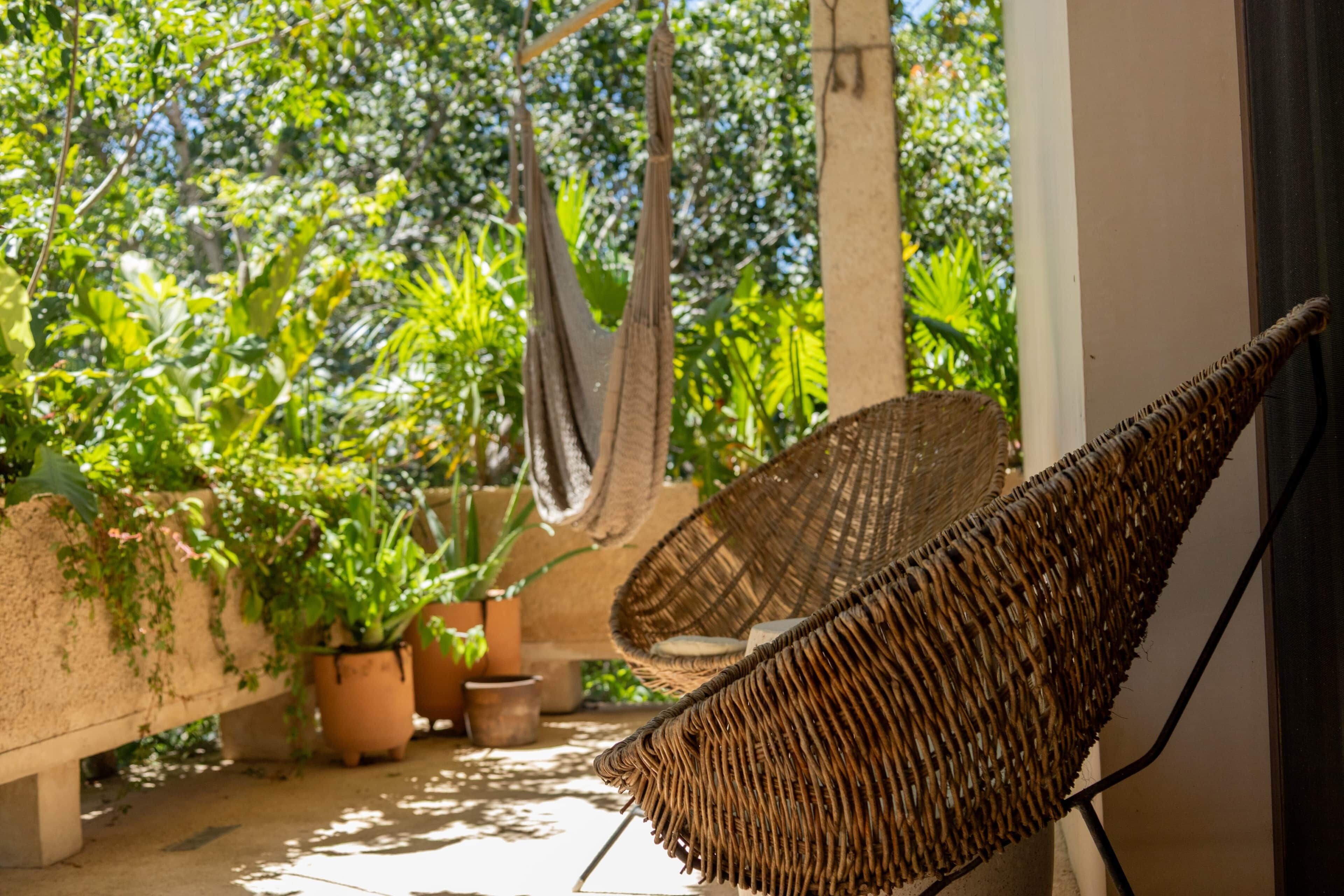 A hammock chair and potted plants on a balcony with a view of greenery.