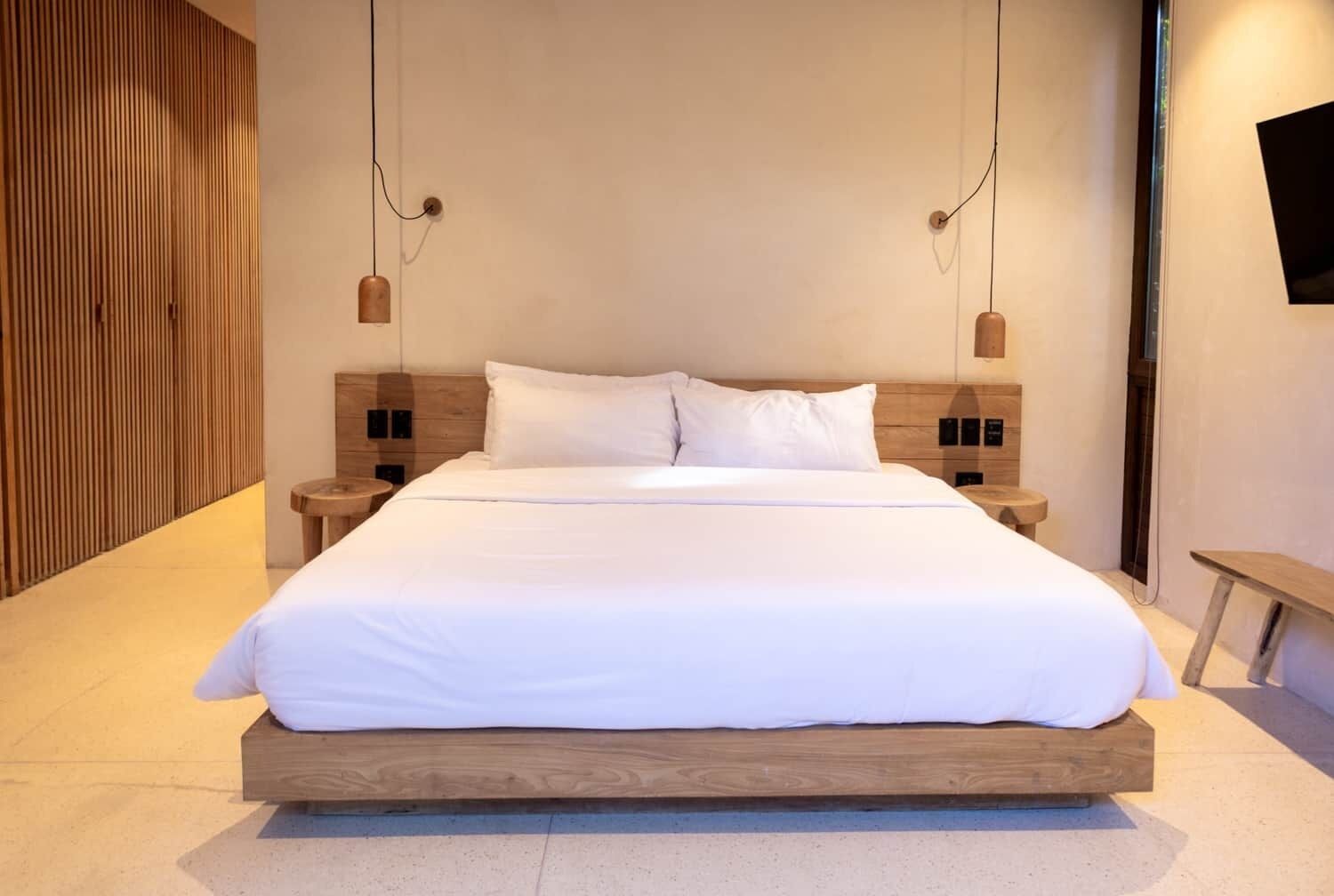 A modern hotel room with a large bed, wooden headboard, and two bedside tables with lamps.