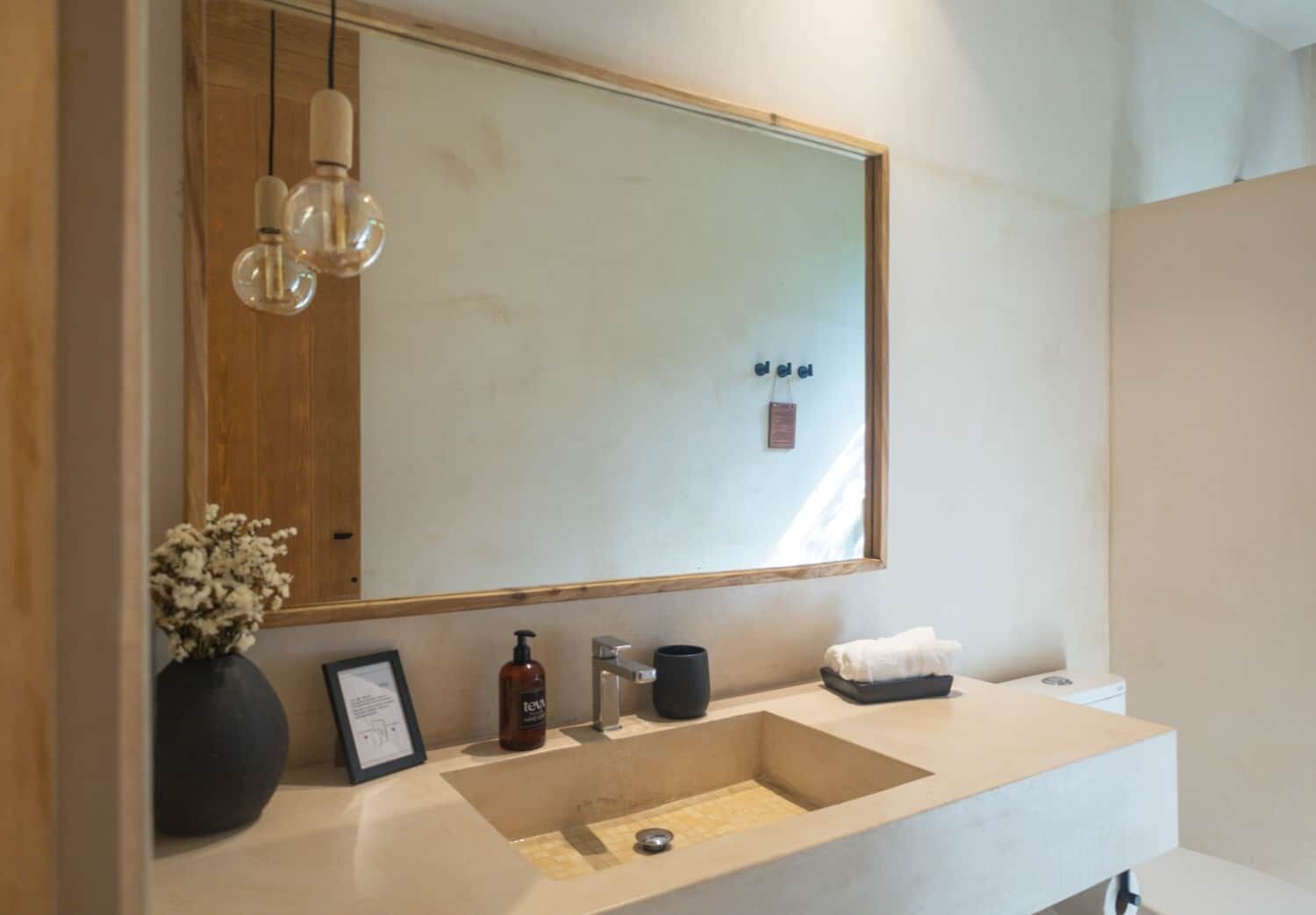 A modern bathroom with a large mirror, a sink with a basin, a framed picture, a bottle of soap, and a towel on the counter.