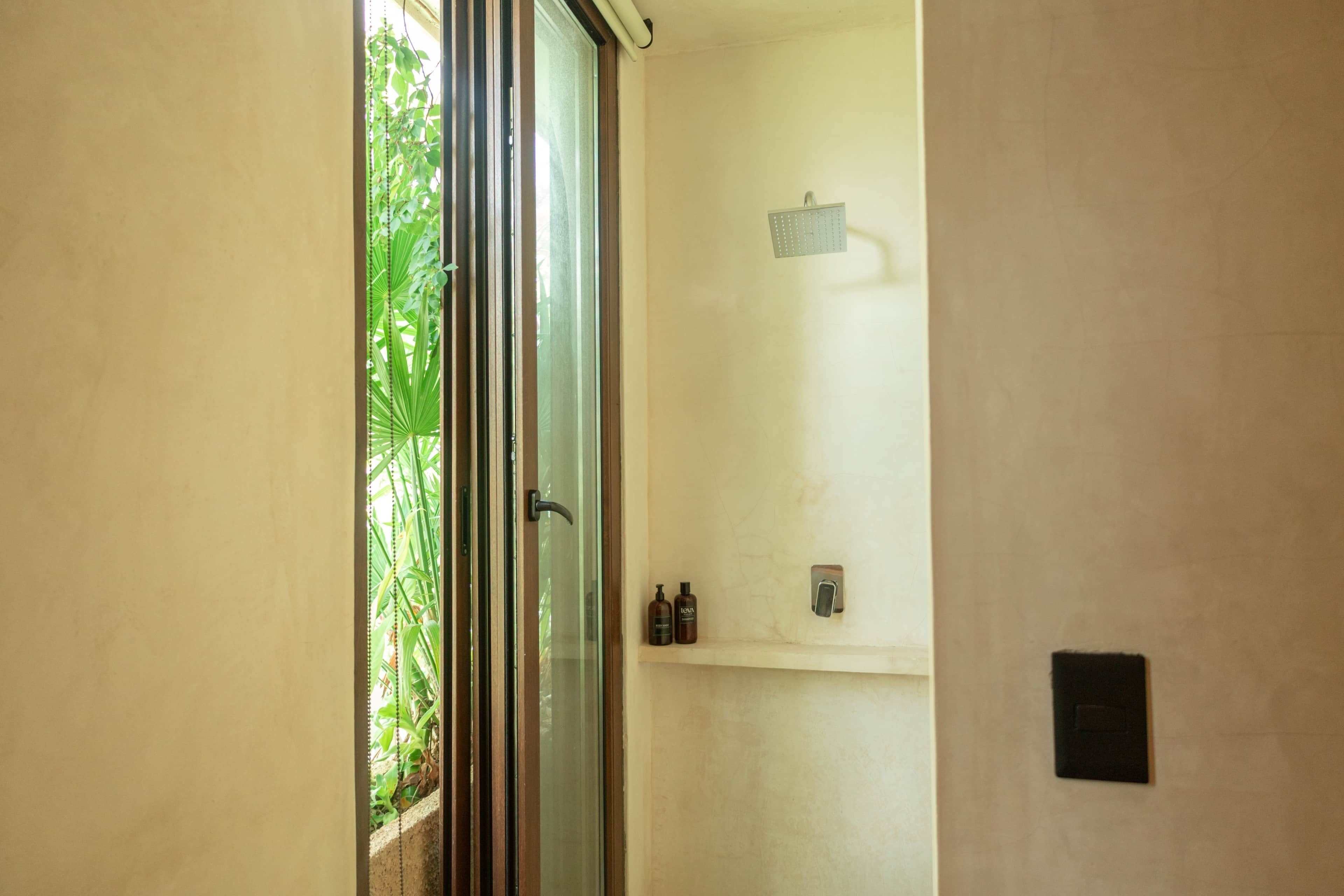 A bathroom with a glass door, a showerhead, and two bottles on a shelf.