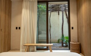A room with a bed, a wooden bench, a sliding glass door, and a wicker basket.