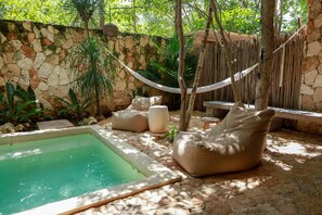 A pool area with a stone wall, a hammock, and beige bean bags.