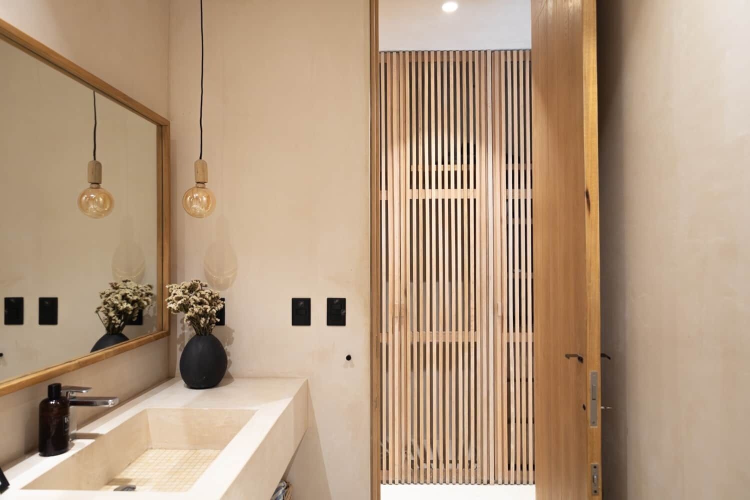 A modern bathroom with a large mirror, a sink, and a wooden partition.