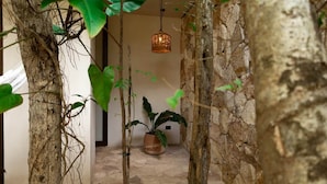 A room with a stone wall, a hanging light fixture, and potted plants. - Room with Private Pool and Garden |• TEVA 2B (Tulum)