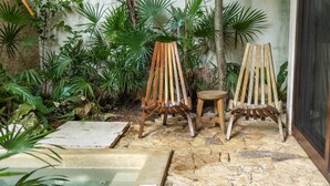 A stone patio with two wooden chairs and a small stool, surrounded by lush green plants. - Room with Private Pool and Garden |• TEVA 2B (Tulum)