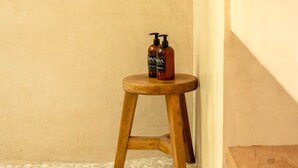 Un taburete de madera con tres botellas de champú y gel de baño frente a una pared lisa.