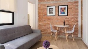 A modern living room with a grey sofa, a small round table with two chairs, and a brick wall with two framed pictures. - Cozy · Cozy apartment great location (Mexico City)